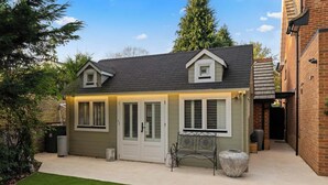 A two-story house with a front porch, a small garden, and a brick wall on the right. - Cosy Alpine Lodge in Claygate (Claygate)