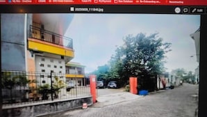 Une vue de rue d’un immeuble dont la façade est jaune et blanche, avec une entrée fermée par un portail et un trottoir dallé.
