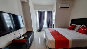 Une chambre d’hôtel avec un lit, une télévision, un bureau et une fenêtre avec des rideaux.