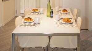 Zona pranzo con tavolo bianco, sedie e lampadario.