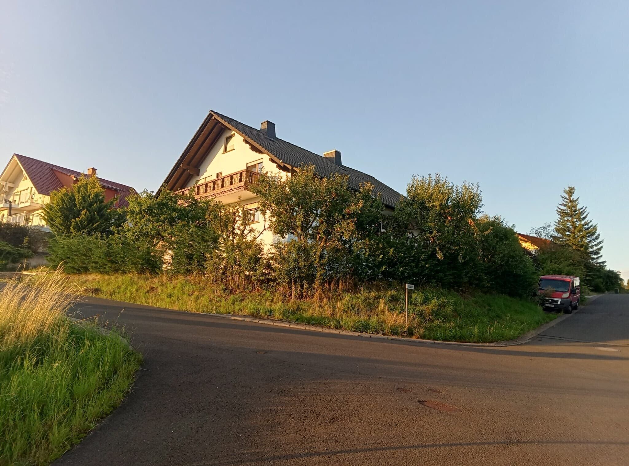 Un quartier résidentiel avec une maison, une route et un véhicule rouge garé sur le bord.