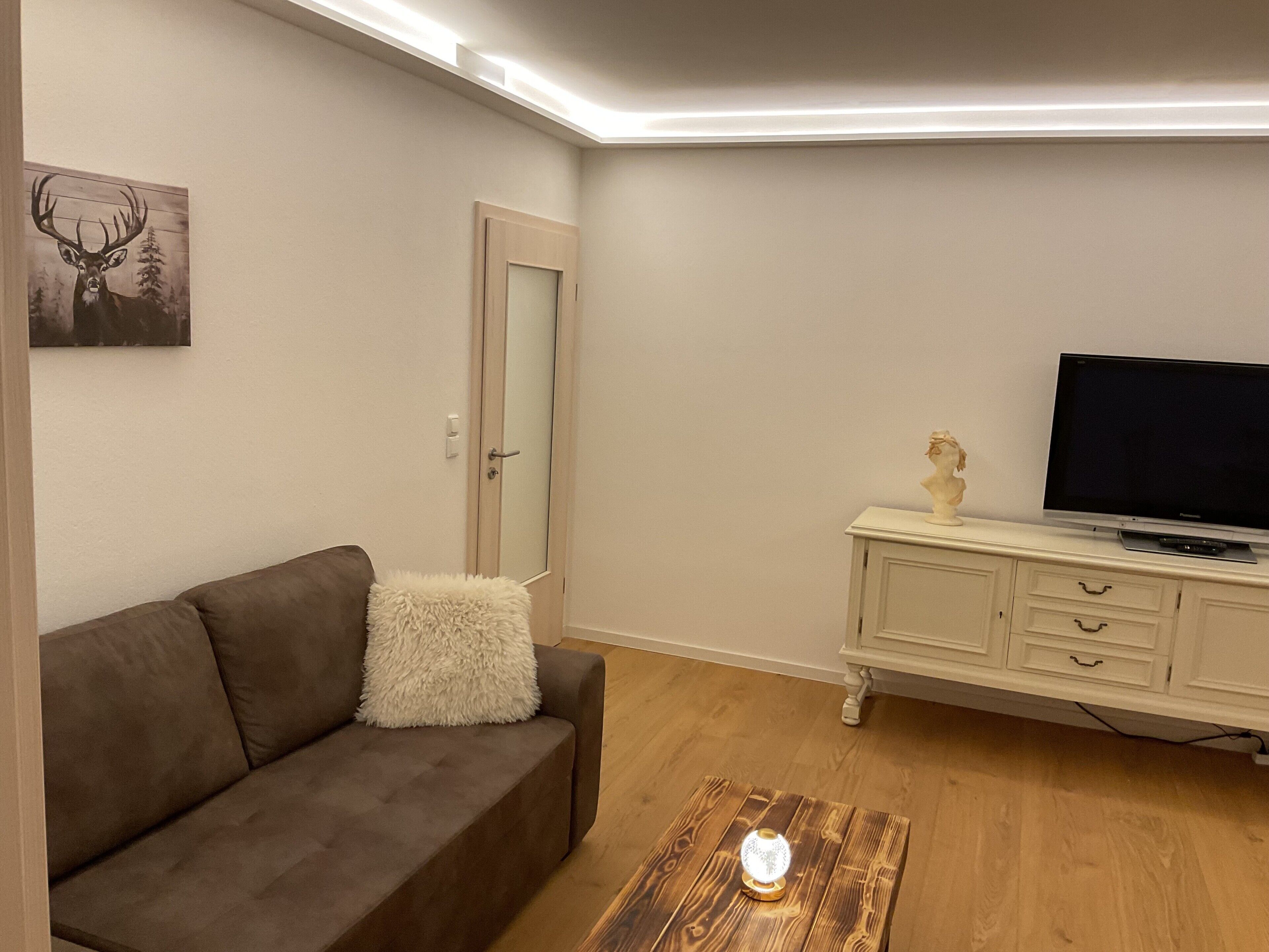 Una sala de estar con un sofá, un televisor sobre un mueble, una puerta y un cuadro en la pared.