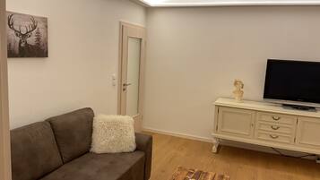 Una sala de estar con un sofá, un televisor sobre un mueble, una puerta y un cuadro en la pared.