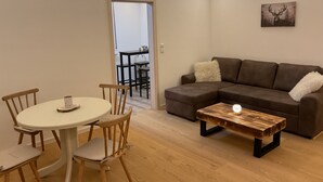 Un salón con un sofá marrón, una mesa de comedor redonda con sillas, una mesa de centro de madera y un cuadro de un ciervo en la pared.