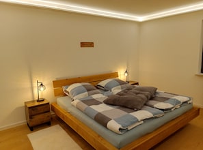 Un dormitorio con una cama de madera, dos mesitas de noche con lámparas, una mesita auxiliar de madera y un cartel en la pared.