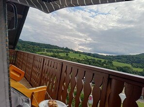 Un balcon donnant sur un paysage verdoyant et un ciel nuageux.