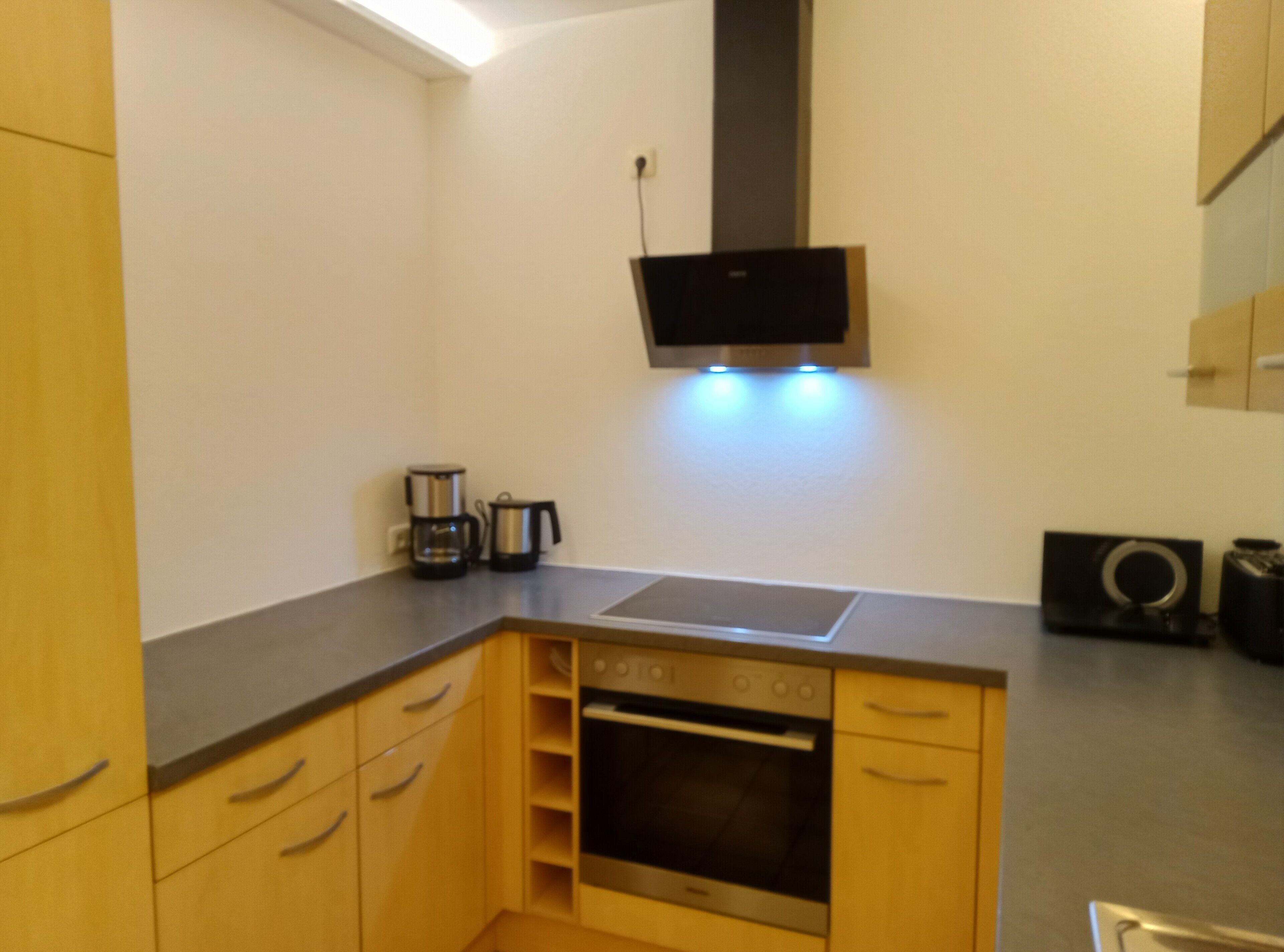 Een compacte keuken met houten kastjes, een inbouwoven, een magnetron en een koffiezetapparaat.
