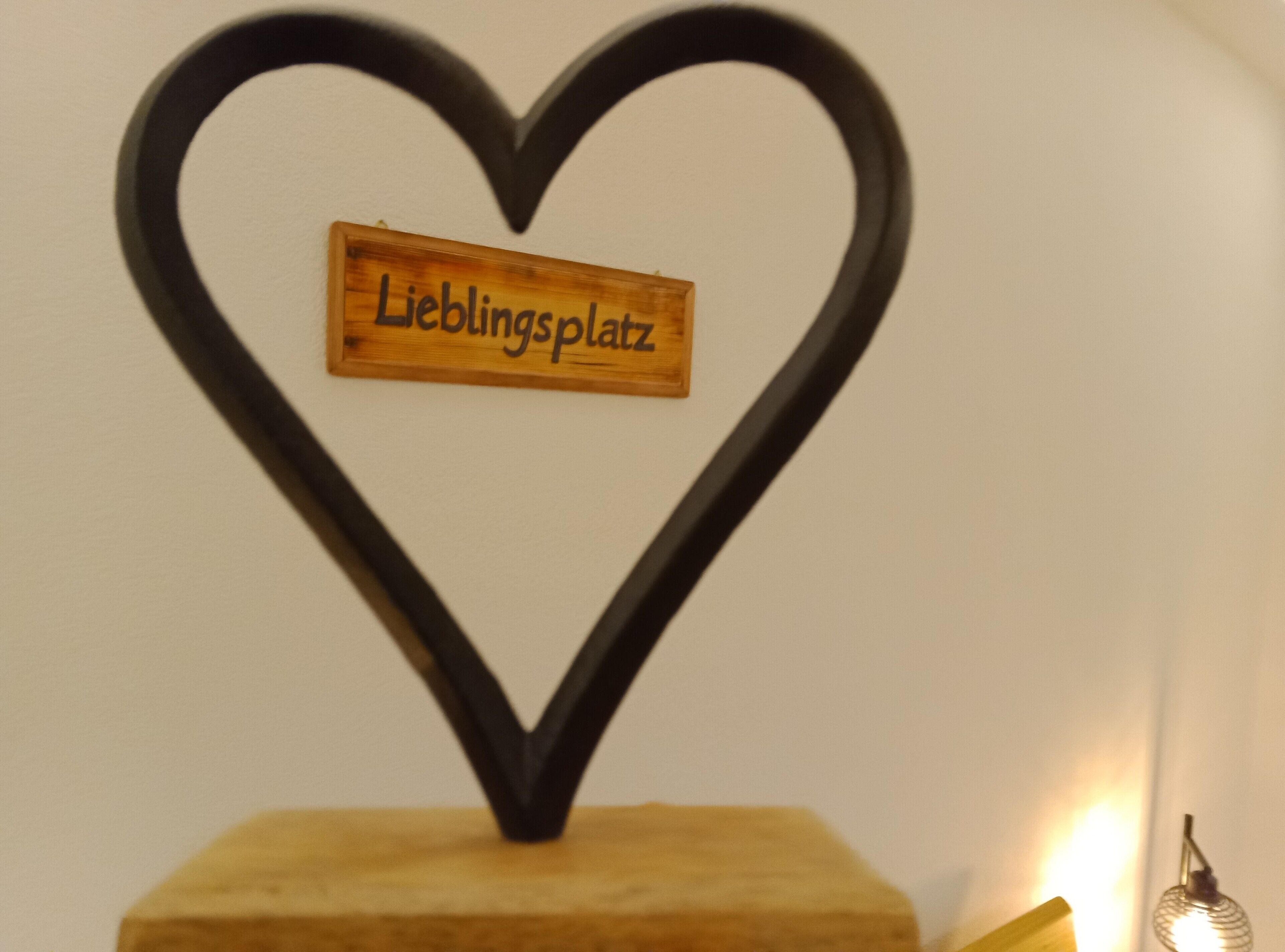 Segno a forma di cuore con su scritto 'Lieblingsplatz', fissato su una base di legno.