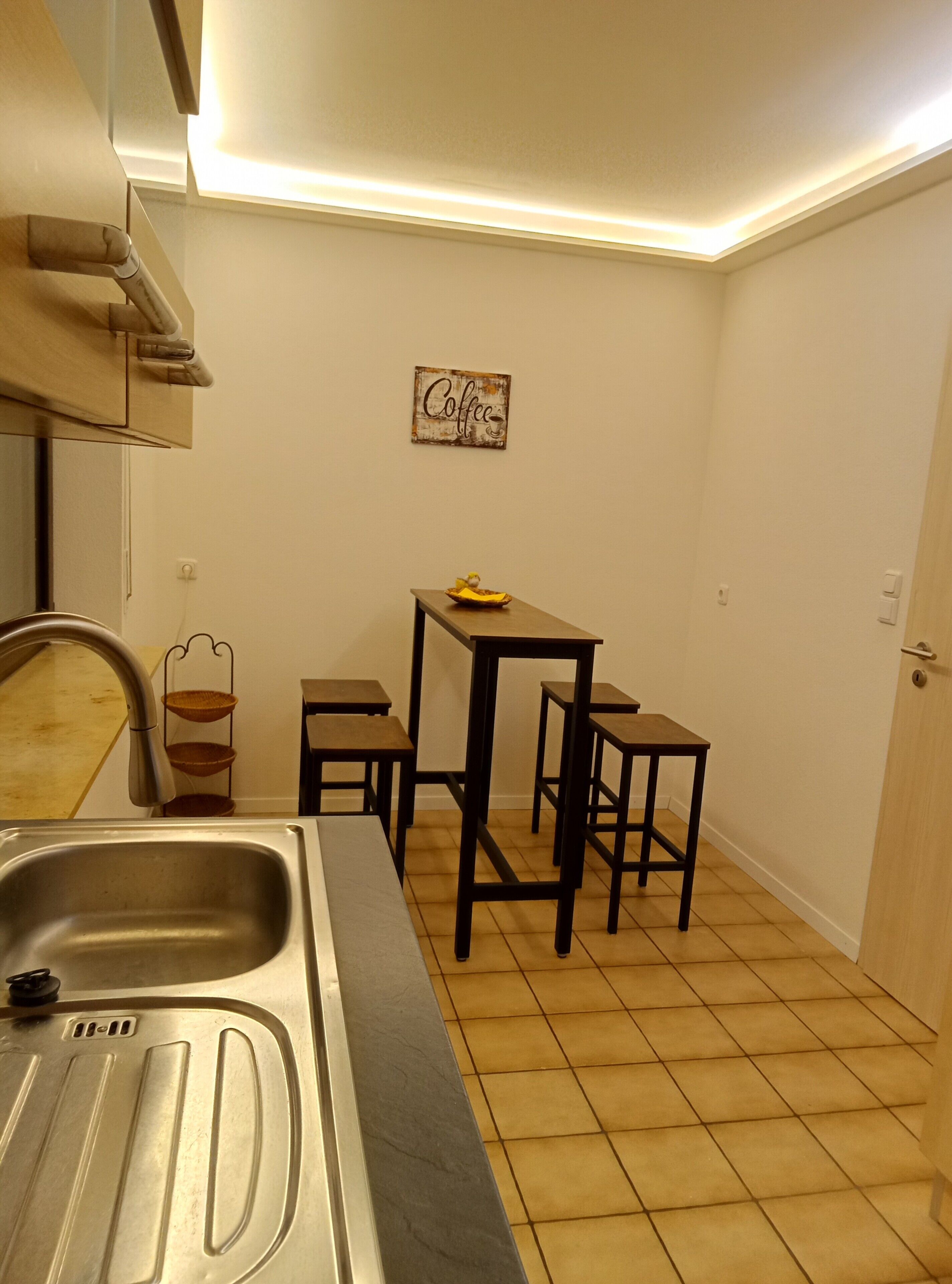 Cozinha com pia, uma pequena mesa com bancos, um letreiro fixado na parede e uma porta.