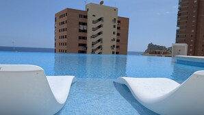 A swimming pool with white lounge chairs, a building in the background, and a clear sky. - SUNSET SAILORS magic apartment (Benidorm)