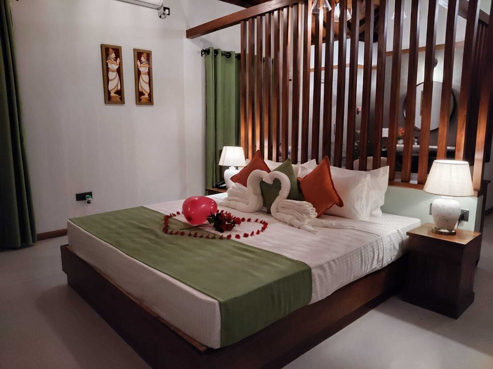 A hotel room with a bed, pillows, a nightstand, a lamp, and a green curtain.