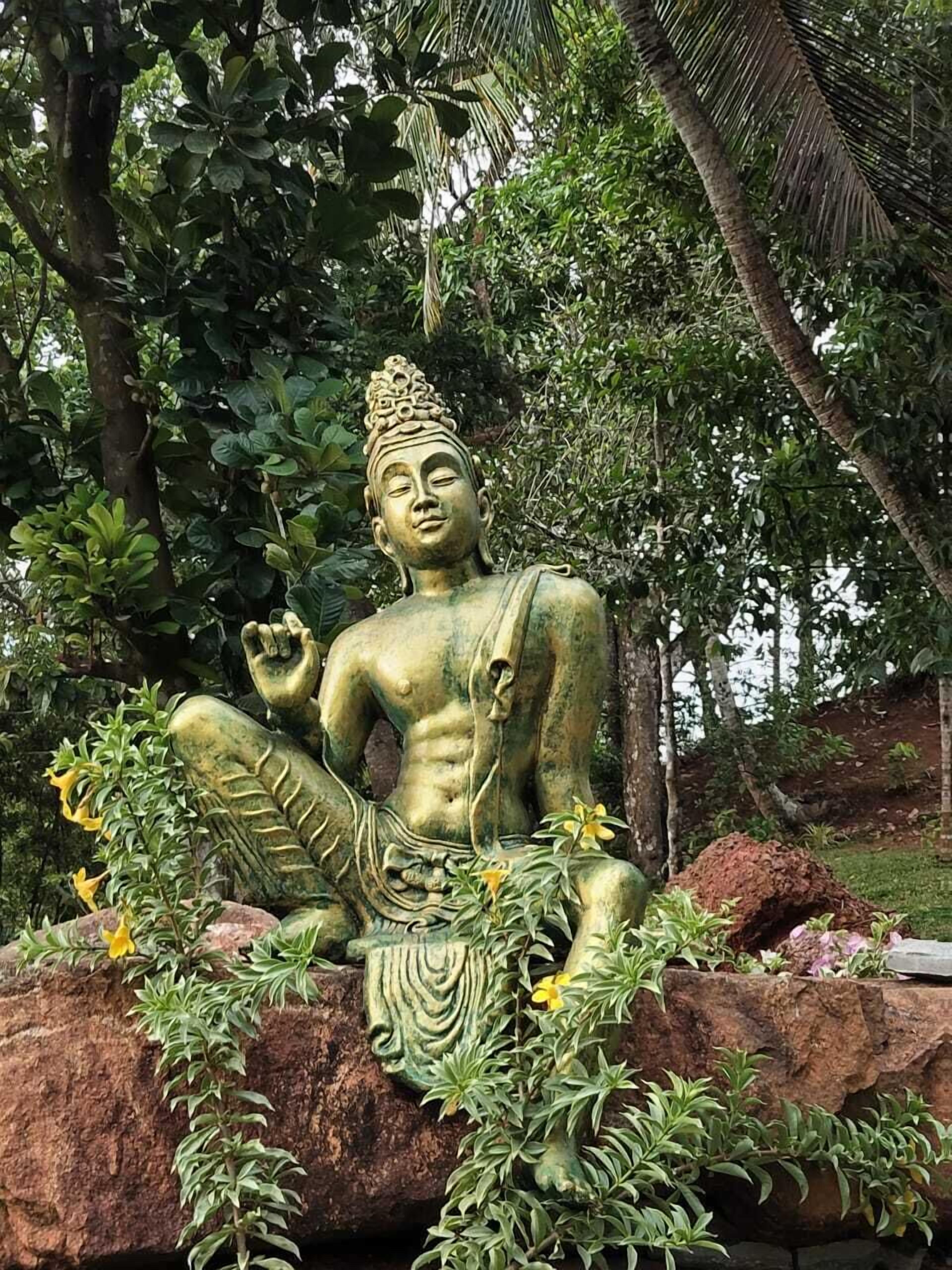Eine sitzende Statue einer Figur inmitten einer natürlichen Umgebung mit Bäumen und Pflanzen.