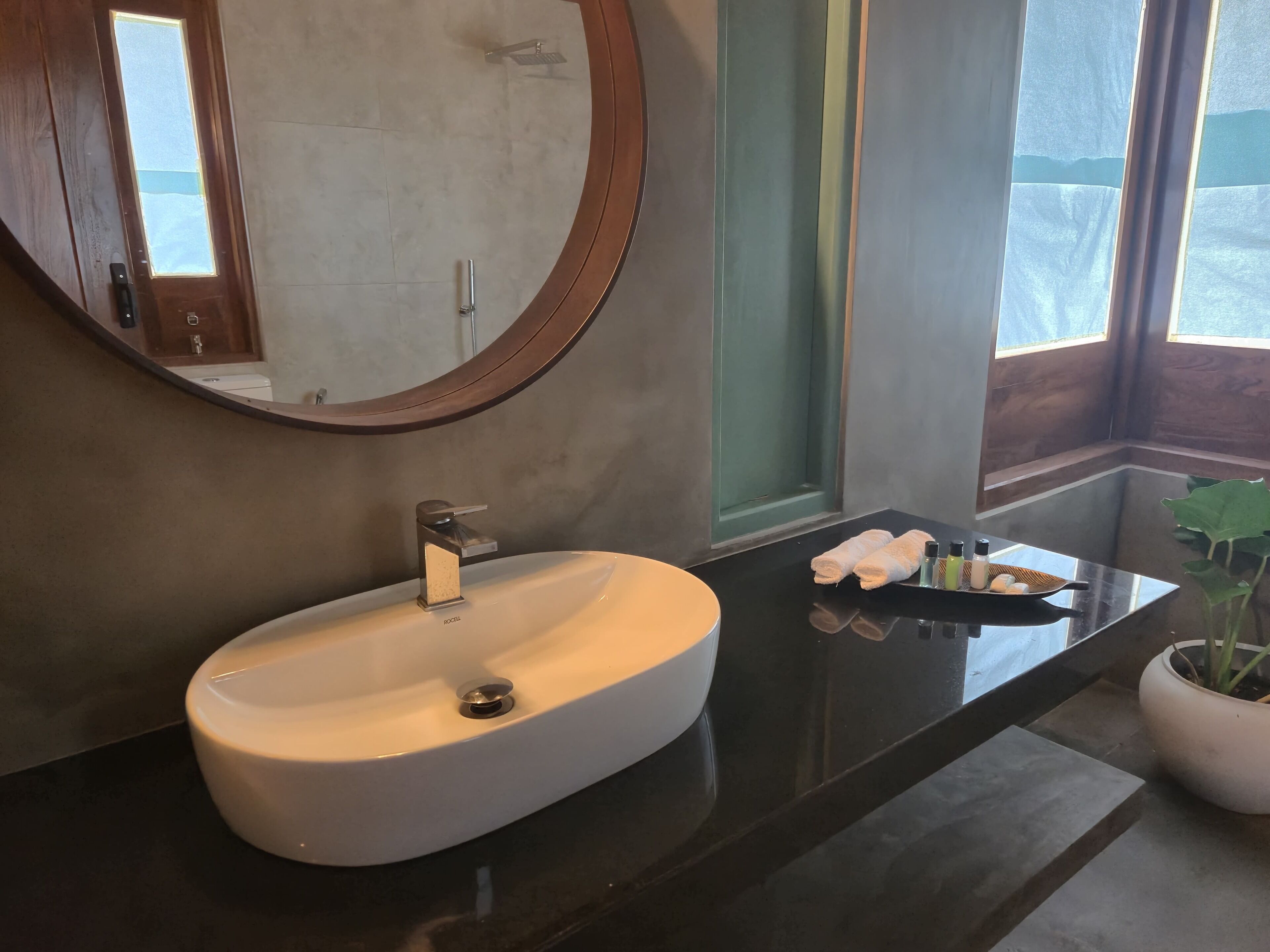 Un baño moderno con un espejo redondo, un lavabo blanco y una encimera negra.