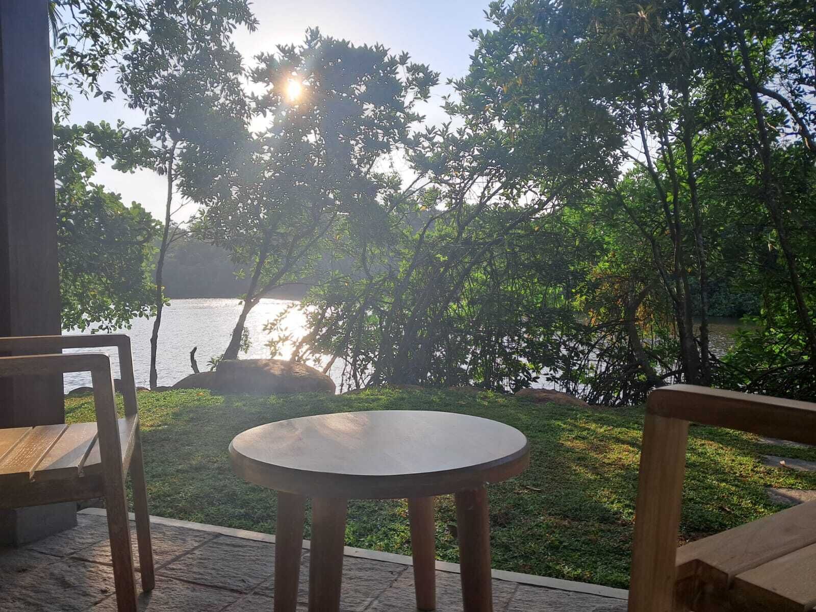 Un tavolo rotondo e due sedie di legno in un'area giardino con vista su un lago e alberi.