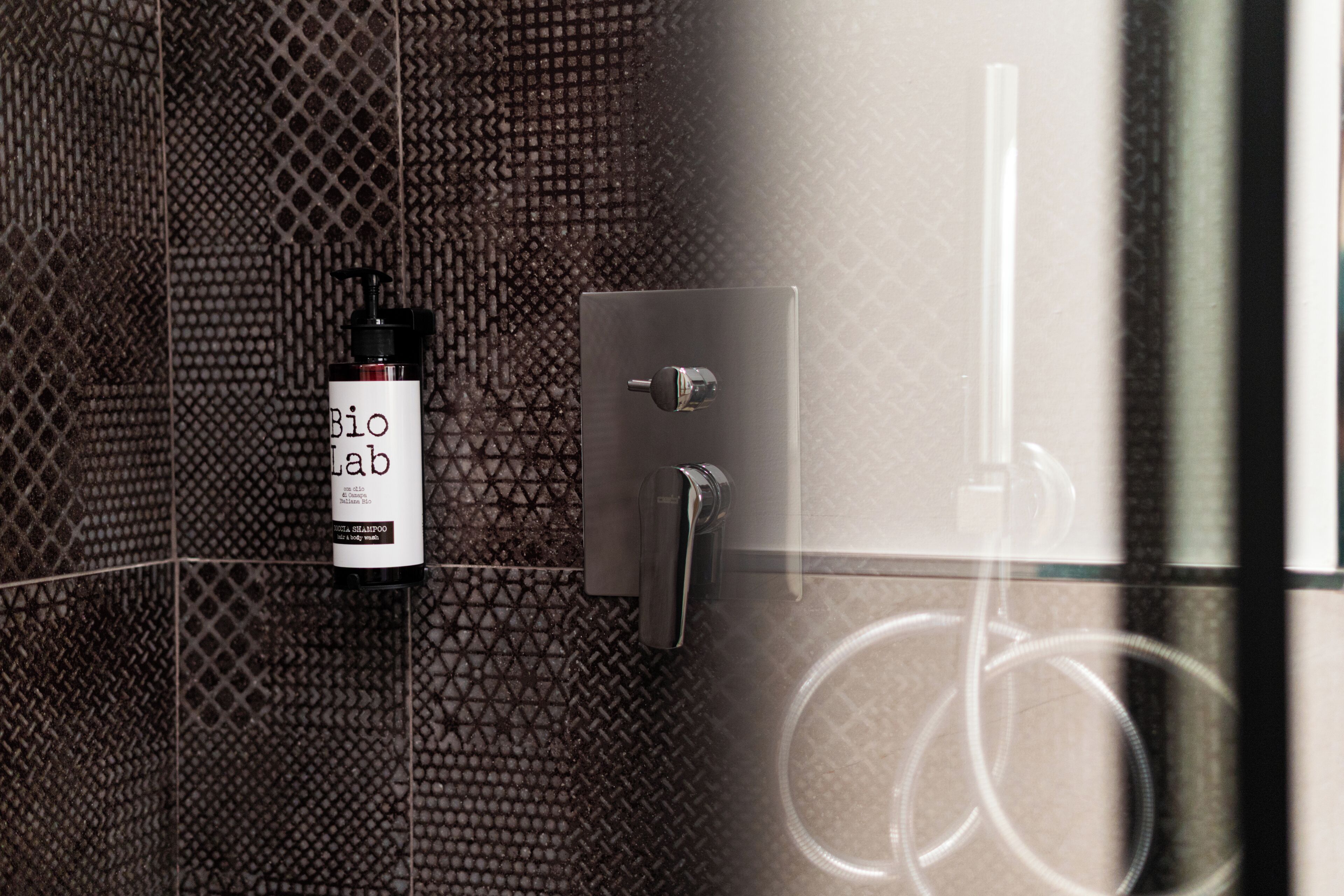 A bathroom with a textured wall, a shampoo bottle, and a faucet.