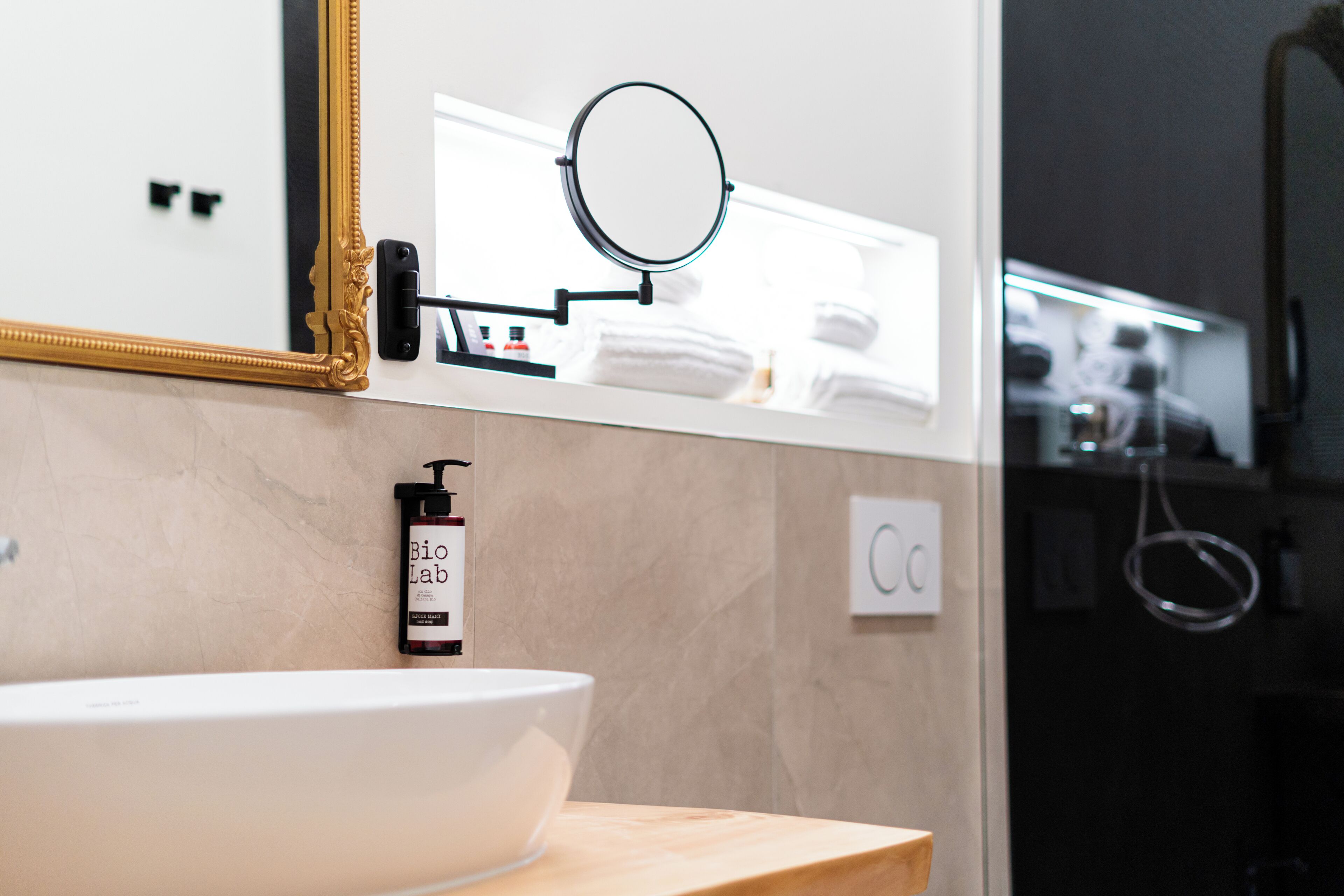 A bathroom with a white sink, a gold-framed mirror, a round mirror, and a bottle of Bio Lab soap.