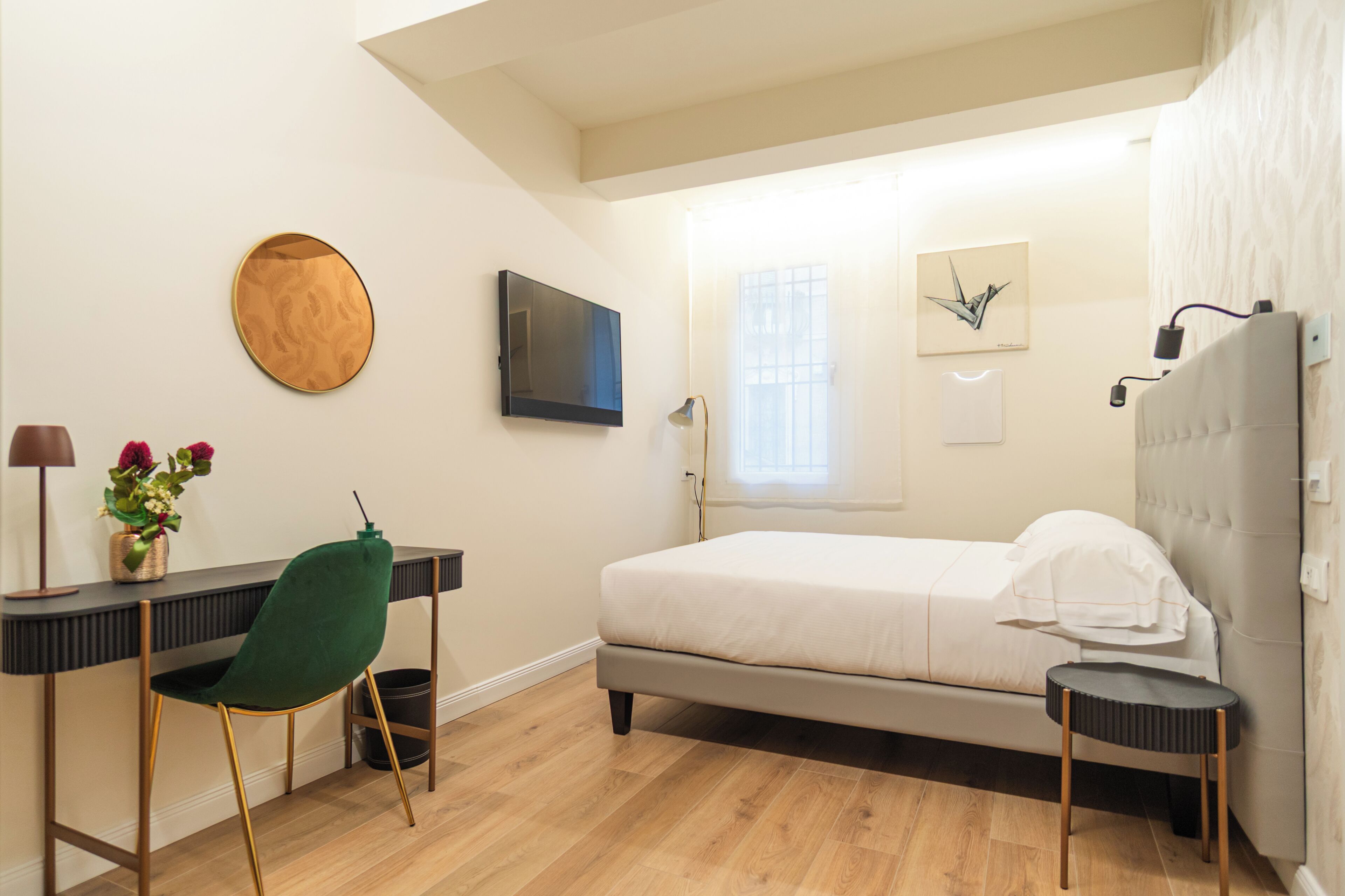 A bedroom with a bed, a desk, a chair, a TV, and a window.