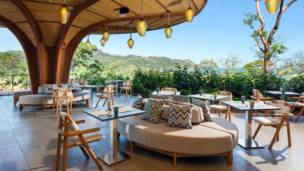 An outdoor seating area with round tables and cushioned seating, surrounded by a wooden pergola with hanging lights. - Spacious 3‑Bed Villa at Reserva Conchal (Cabo Velas)
