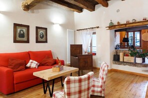 A room with a red sofa, a wooden table, a plaid chair, a wooden cabinet, and a window with curtains. - Room 'Unità 1' with Lake View, Wi-Fi, and Air Conditioning (Fratta)