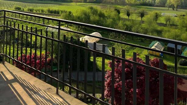 A balcony with a metal railing overlooking a green landscape with trees and a distant town. - Room 'Unità 1' with Lake View, Wi-Fi, and Air Conditioning (Fratta)