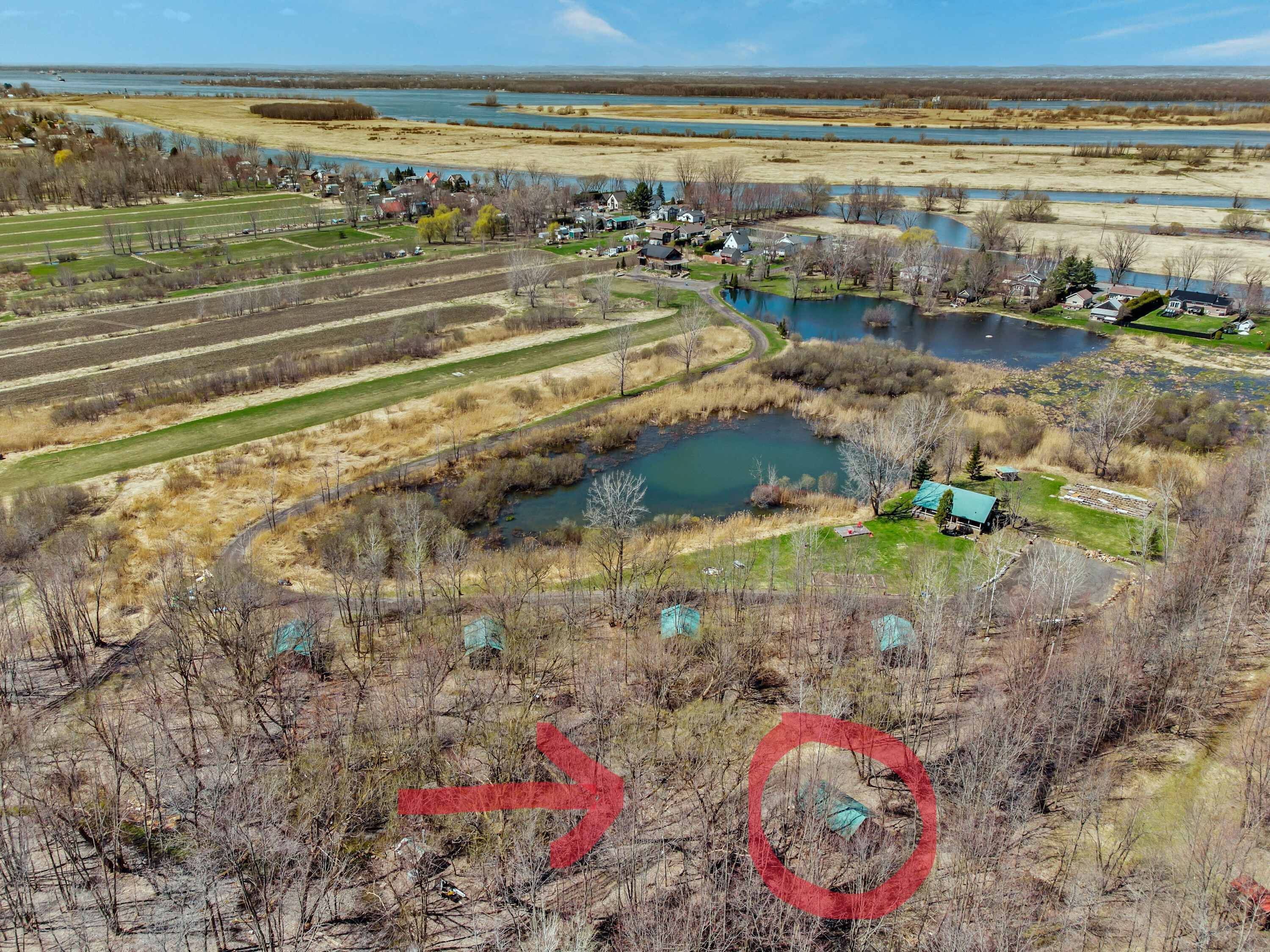 An aerial view of a rural area with fields, a small lake, and a few houses.