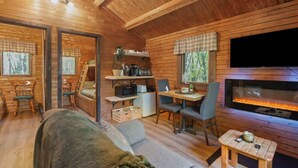 A cozy cabin interior with a fireplace, wooden walls, a dining area, and a sofa. - Mini Chalet # 5  Domaine de lArchipel (Montérégie)