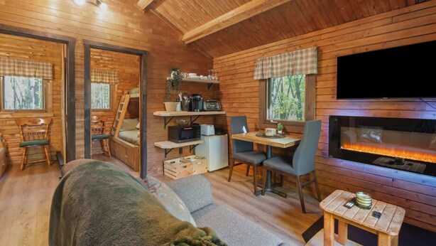 A cozy cabin interior with a fireplace, wooden walls, a dining area, and a sofa. - Mini Chalet # 2  Domaine de l Archipel (Montérégie)