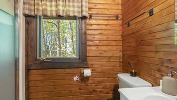 A wooden cabin bathroom with a window, toilet, sink, and towel rack.