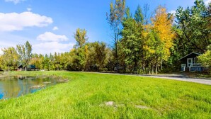 A grassy area with a pond and trees, a small building with a porch, and a clear sky. - Mini Chalet # 2  Domaine de l Archipel (Montérégie)