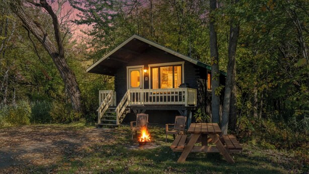 Una cabaña con terraza, una fogata y mobiliario exterior.
