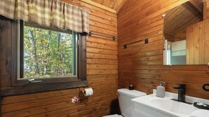 Baño de cabaña de madera con inodoro, lavamanos y ventana.