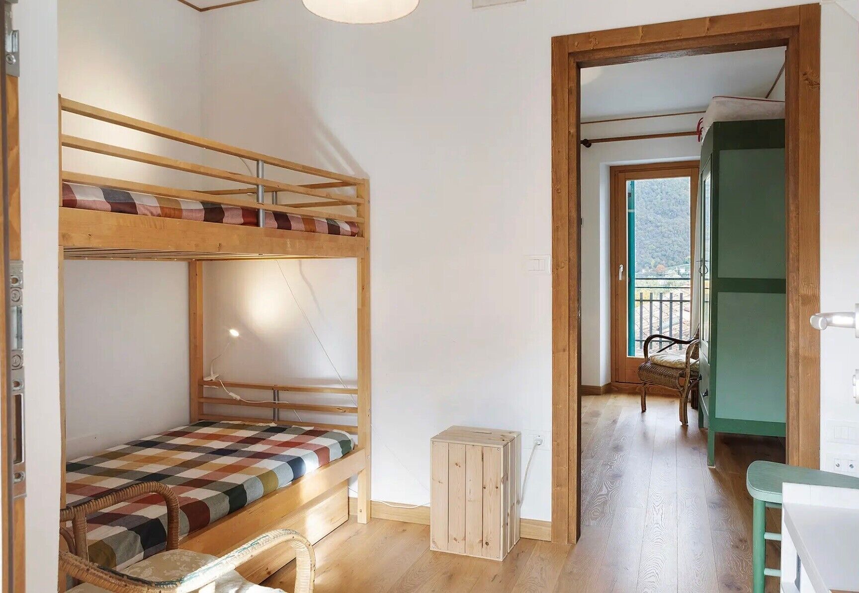 A bunk bed with a checkered bedspread, a small wooden stool, and a chair.