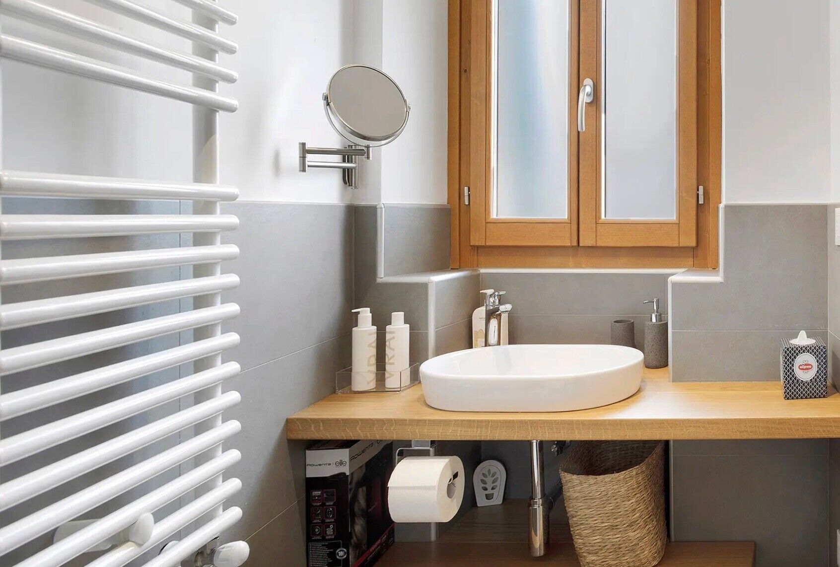 A bathroom with a white sink, wooden vanity, a round mirror, and a towel rack.