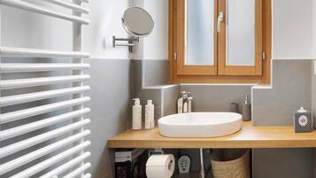 A bathroom with a white sink, wooden vanity, a round mirror, and a towel rack.