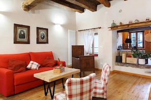 Quarto com sofá vermelho, mesa de madeira, cadeira xadrez, armário de madeira e janela com cortinas.