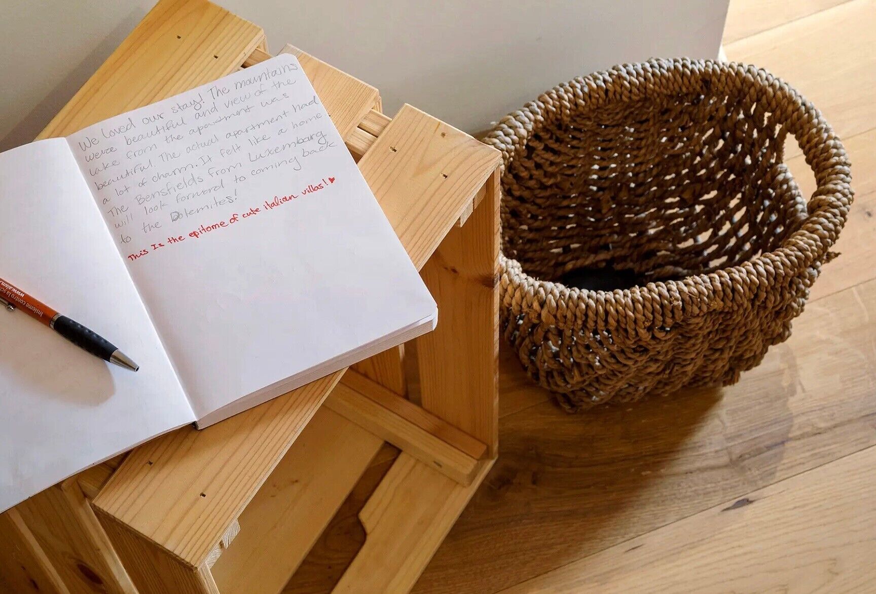An open notebook with handwritten notes on a wooden table, a pen, and a woven basket beside it.