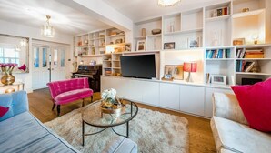 Un salon spacieux doté d’un téléviseur à écran plat, d’un piano et d’une bibliothèque remplie de livres et d’objets décoratifs.