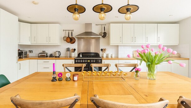 Une cuisine moderne avec des armoires blanches, une cuisinière en acier inoxydable et une table à manger avec des chaises.