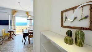 Een kamer met een eethoek, een witte console tafel met decoratieve cactussen, en uitzicht op de zee door een glazen deur.
