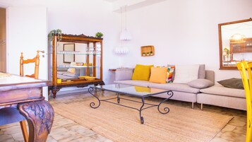 Una sala de estar con sofá, mesa de centro de vidrio, mesita de noche de madera y espejo.