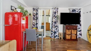 Ein kompakter Wohnraum mit einem roten Kühlschrank, einem Esstisch mit Stühlen, einem Fernseher und einem Surfbrett.