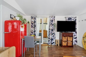 A compact living space with a red refrigerator, a dining table with chairs, a television, and a surfboard.