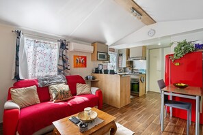 A compact living space with a red sofa, a wooden coffee table, a kitchen area, and a dining table with a red refrigerator.