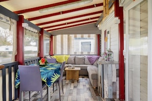 A covered porch with a table and chairs, a sofa, and a small table with a flower vase.