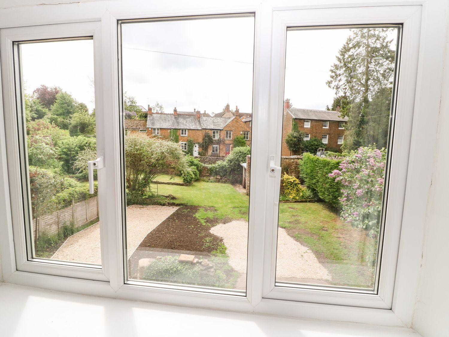 A view through a window with a garden and houses in the background.