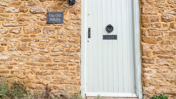 A stone building with a white door and a sign reading "The Old Bakery". - The Old Bakery (Banbury)