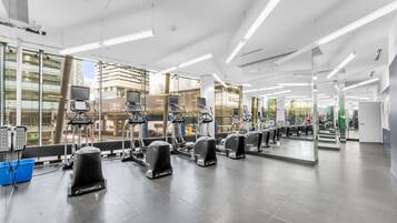 Academia moderna com equipamentos de cardio, espelhos e amplas janelas.