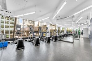 Academia moderna com equipamentos de cardio, espelhos e amplas janelas.