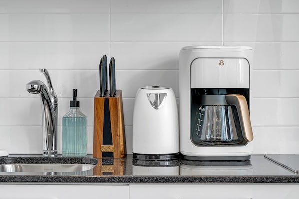 Uma cozinha moderna com uma pia de aço inoxidável, uma cafeteira e um porta-facas.