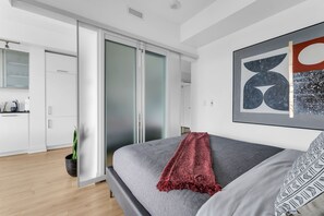 A modern bedroom with a grey bed, a red throw blanket, and a large abstract painting on the wall. - Aurelien Toronto (Toronto)